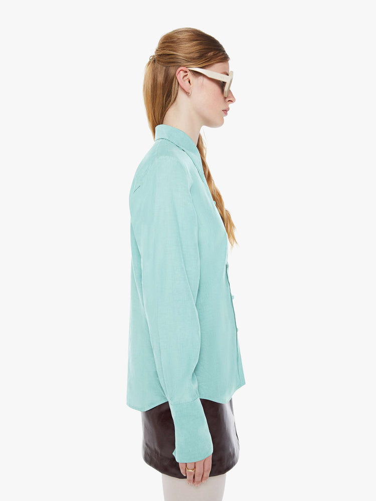 Side view of a woman in light turquoise blue button-up with a pointed collar, long balloon sleeves, extra-wide cuffs at the wrists.