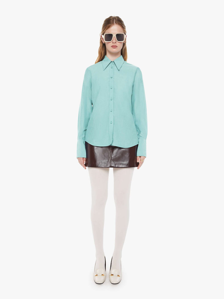 Full body view of a woman in light turquoise blue button-up with a pointed collar, long balloon sleeves, extra-wide cuffs at the wrists.