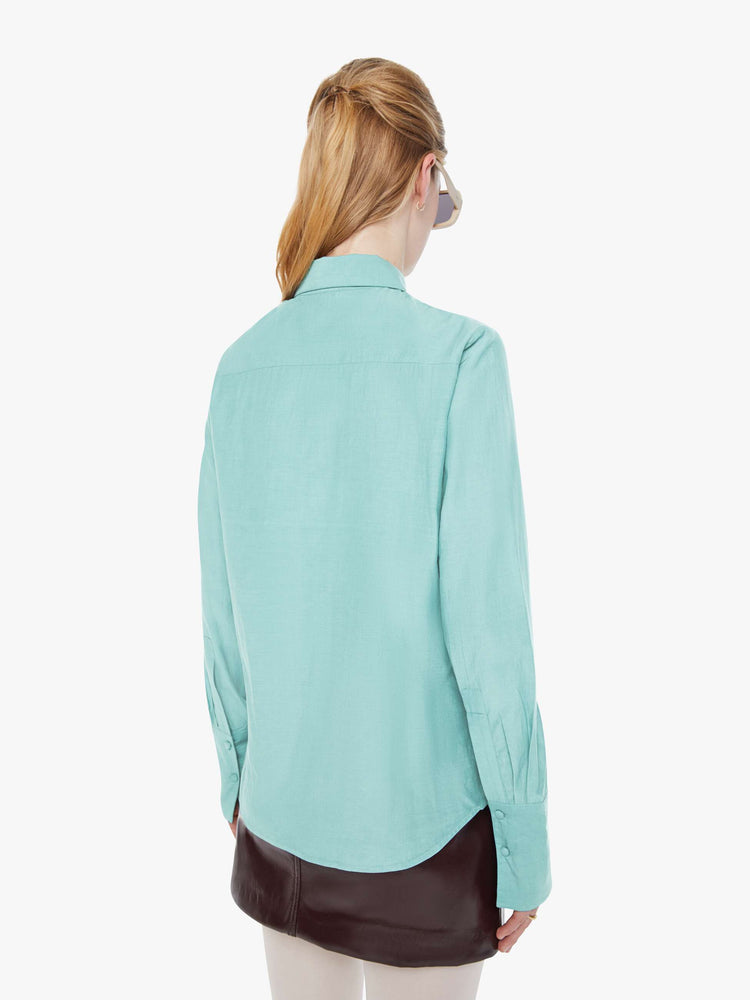 Back view of a woman in light turquoise blue button-up with a pointed collar, long balloon sleeves, extra-wide cuffs at the wrists.