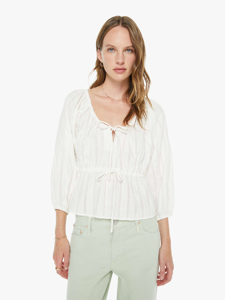 Front view of a woman in a white scoopneck blouse with 3/4-length balloon sleeves, ruffles throughout, tied details at the neck and waist and a slightly cropped hem.