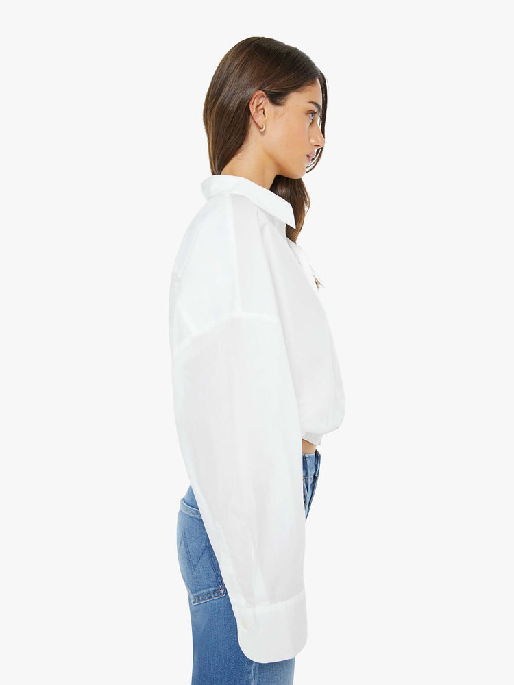 Side view of woman in a white cropped button-up with long wide sleeves and a bubble hem.