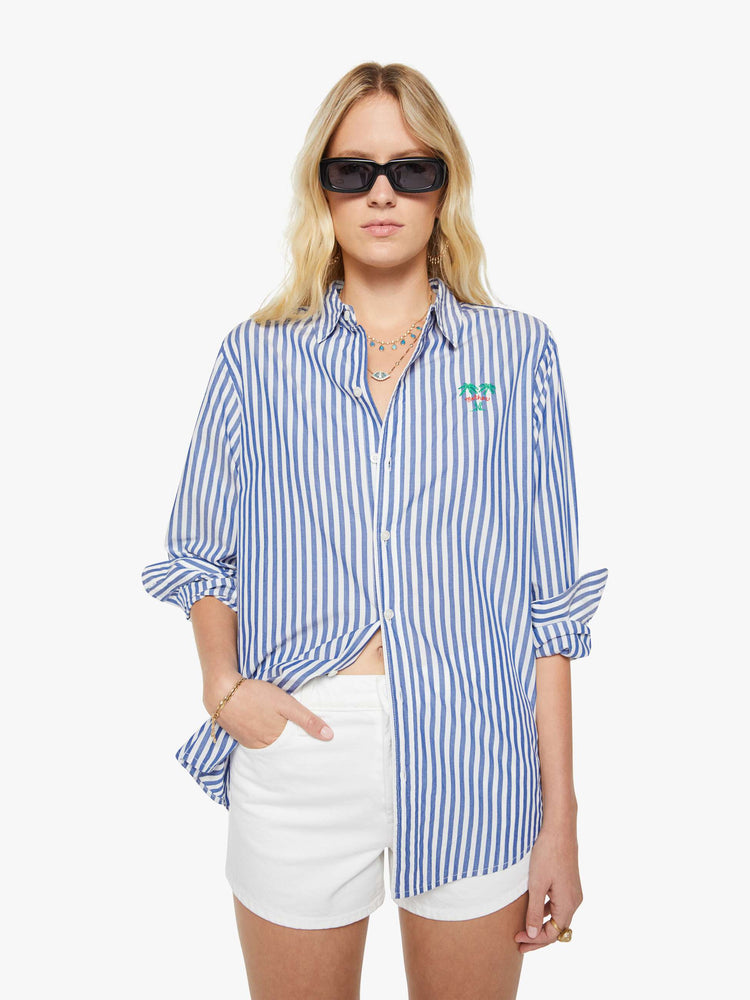 Front view of a woman in a blue and white stripes button-up shirt with a curved hem and MOTHER's name embroidered with two small palm trees on the chest.