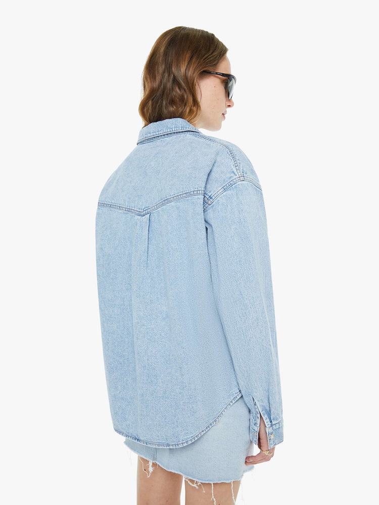 Back view of a woman in a denim button-up with drop shoulders, a front patch pocket and faux-pearl snaps down the front.