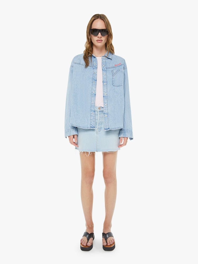 Full body view of a woman in a denim button-up with drop shoulders, a front patch pocket and faux-pearl snaps down the front.