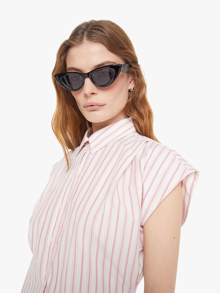Close up view of a light pink stripe pattern  short-sleeve button-up with an angled bodice and a curved hem. 