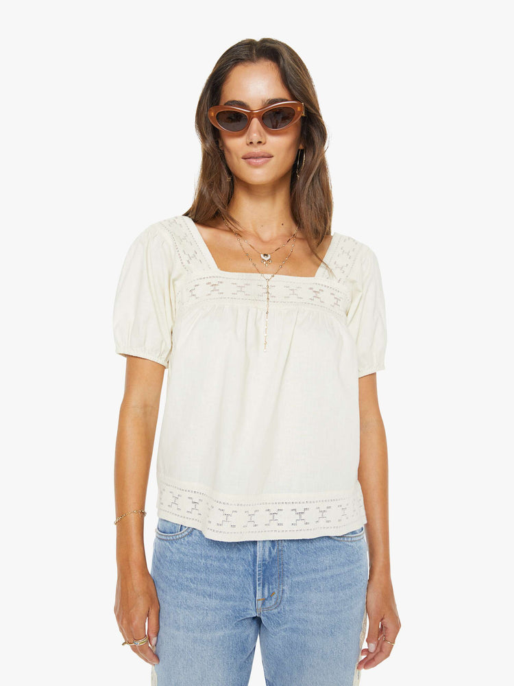 Front view of a woman in an off white square-neck blouse with short puff sleeves and a loose, flowy fit.