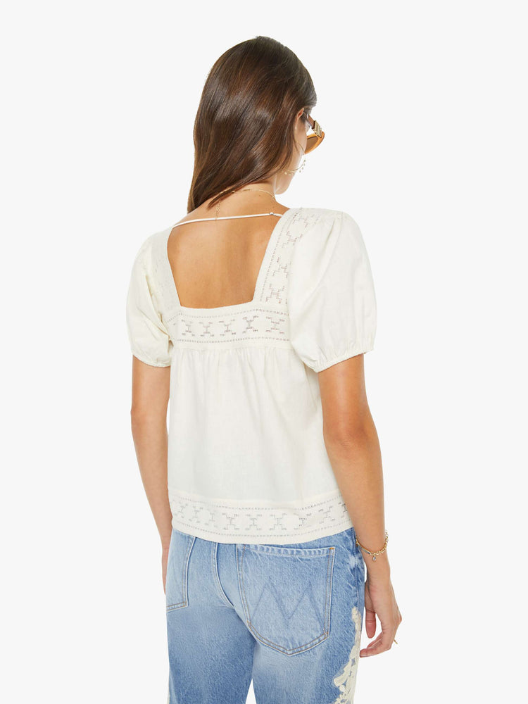 Back view of a woman in an off white square-neck blouse with short puff sleeves and a loose, flowy fit.