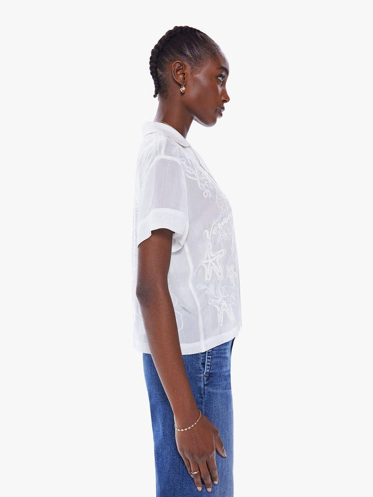 Side view of a woman's hort-sleeve button-up with a notched collar and boxy fit in a sheer white hue.