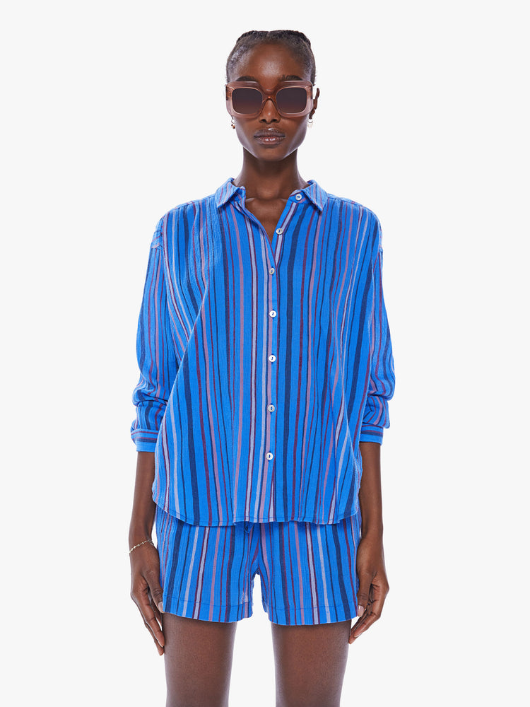 Front view of a women blue stripe pattern button down top with drop shoulders, a curved hem and a slightly oversized fit. 