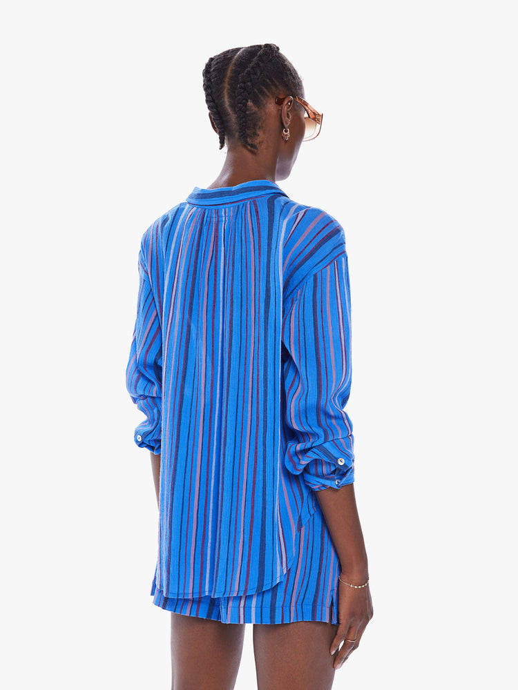 Back view of a women blue stripe pattern button down top with drop shoulders, a curved hem and a slightly oversized fit.