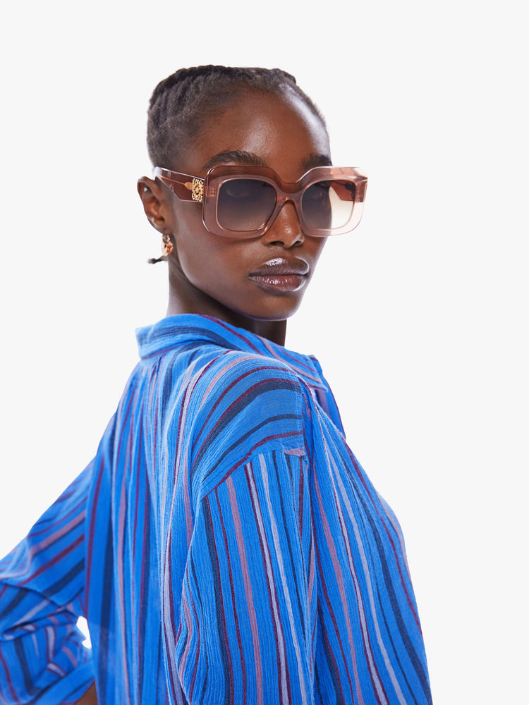 Close up view of a women blue stripe pattern button down top with drop shoulders, a curved hem and a slightly oversized fit.