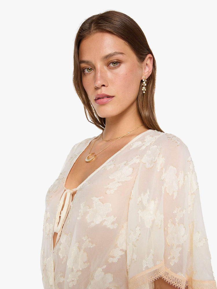 Close up view of woman in a peach lace sheer blouse with a deep V-neck that ties, elbow-length flutter sleeves, an elastic waist and a flowy hem.