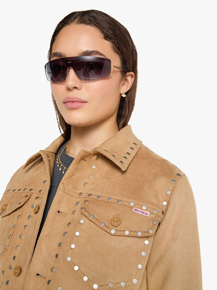 Close up view of a woman in a khaki faux suede jacket features studded details throughout and off-white lining with navy doodles.