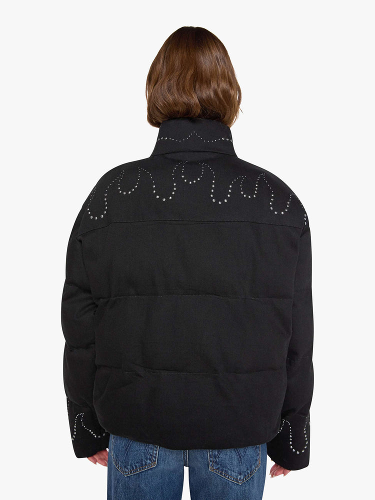 Back view of a woman in a black with flame studded down th middle  boxy puffer jacket with a stacked collar, drop shoulders, slit pockets, a zip closure that buttons and a slightly cropped fit. 