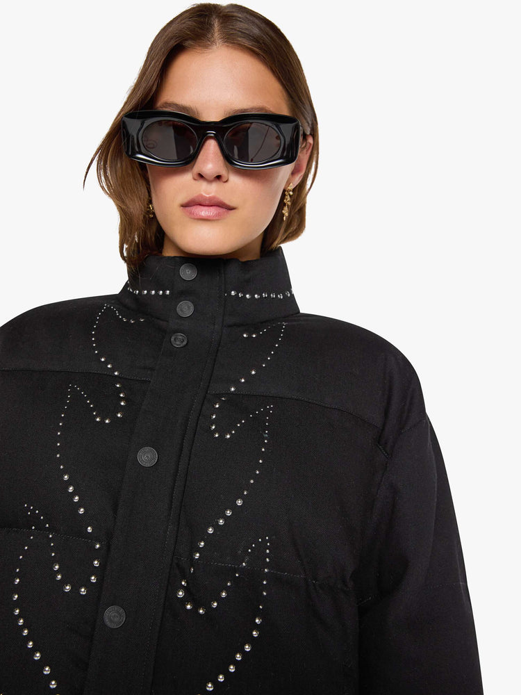 Close up view of a woman in a black with flame studded down th middle  boxy puffer jacket with a stacked collar, drop shoulders, slit pockets, a zip closure that buttons and a slightly cropped fit. 