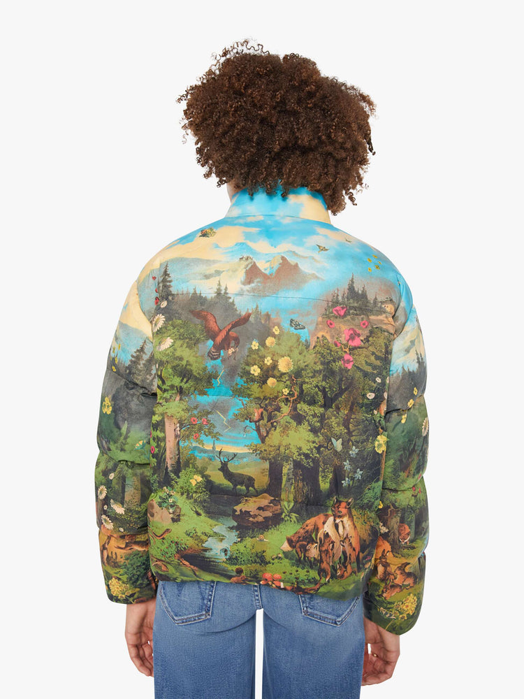 Back view of a woman in a puffer jacket with a high collar, zip and snap closure, slit pockets in a quilted fabric with a colorful pastoral graphic.