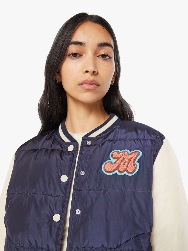 Close up view of navy quilted letterman jacket with a crewneck, snaps down the front, ribbed hems and a slightly cropped fit.