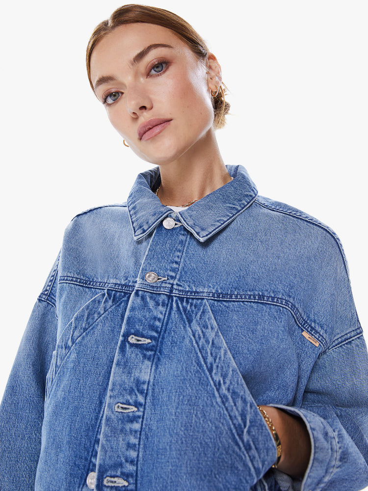 Close up view of woman's denim jacket with drop shoulders, slit pockets at the chest, seamed details and a boxy fit in mid blue wash.