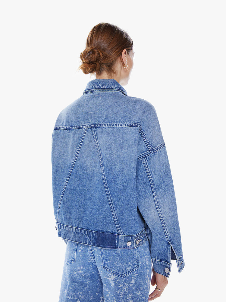 Back view of woman's denim jacket with drop shoulders, slit pockets at the chest, seamed details and a boxy fit in mid blue wash.