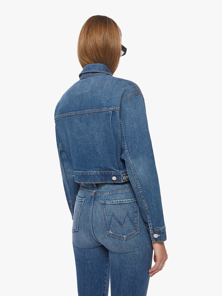 Back view of a dark blue wash denim jacket has a shrunken, boxy fit with oversized patch pockets and a slightly cropped hem.