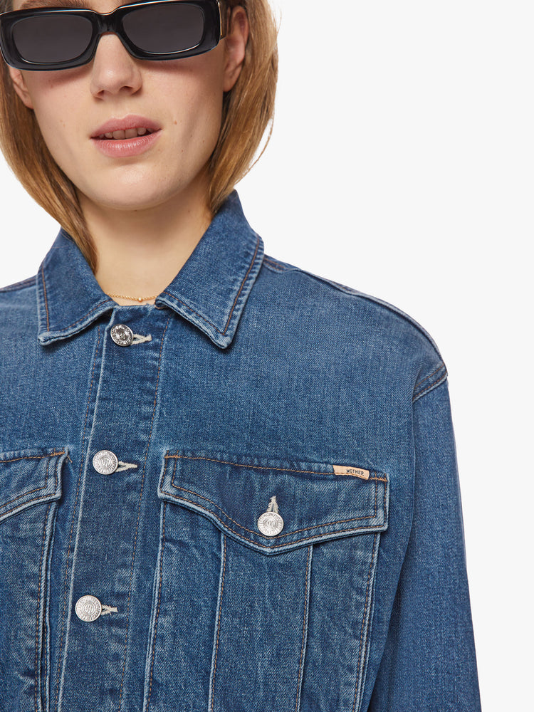 Close up view of a dark blue wash denim jacket has a shrunken, boxy fit with oversized patch pockets and a slightly cropped hem.