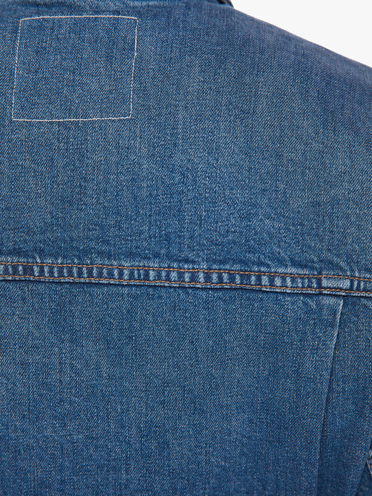 Back close up view of a dark blue wash denim jacket has a shrunken, boxy fit with oversized patch pockets and a slightly cropped hem.