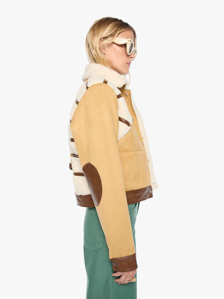 Side view of a woman in a faux-shearling panels at the shoulders, a faux-shearling collar and brown faux-leather trim collared button-up jacket with a cropped hem and a boxy fit. 