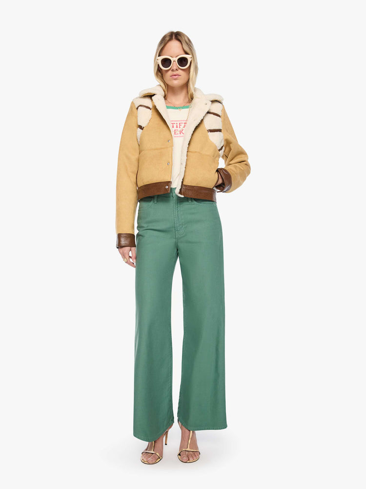 Full body view of a woman in a faux-shearling panels at the shoulders, a faux-shearling collar and brown faux-leather trim collared button-up jacket with a cropped hem and a boxy fit. 
