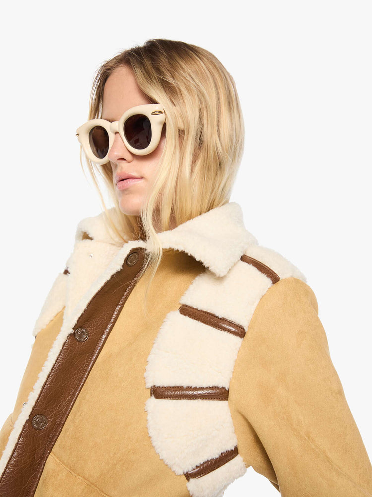 Close up view of a woman in a faux-shearling panels at the shoulders, a faux-shearling collar and brown faux-leather trim collared button-up jacket with a cropped hem and a boxy fit. 