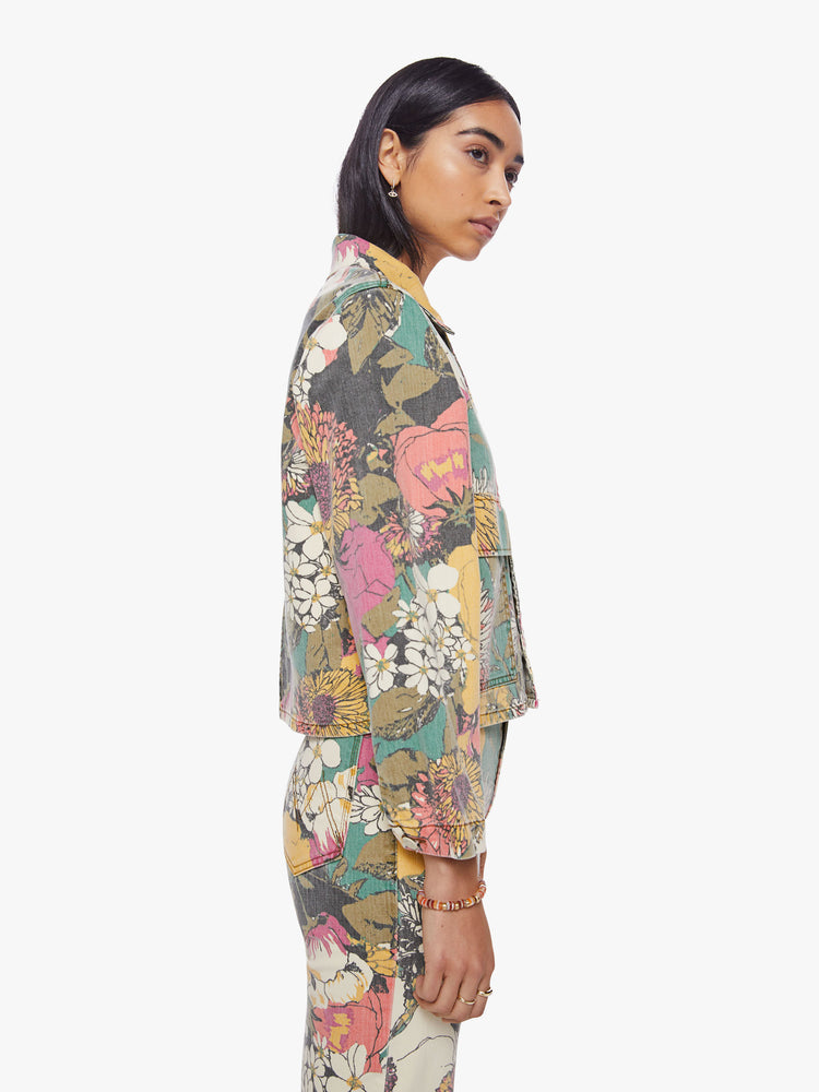 Side view of a woman faded floral print denim jacket with oversized front patch pockets, cropped long sleeves and a boxy, shrunken fit.