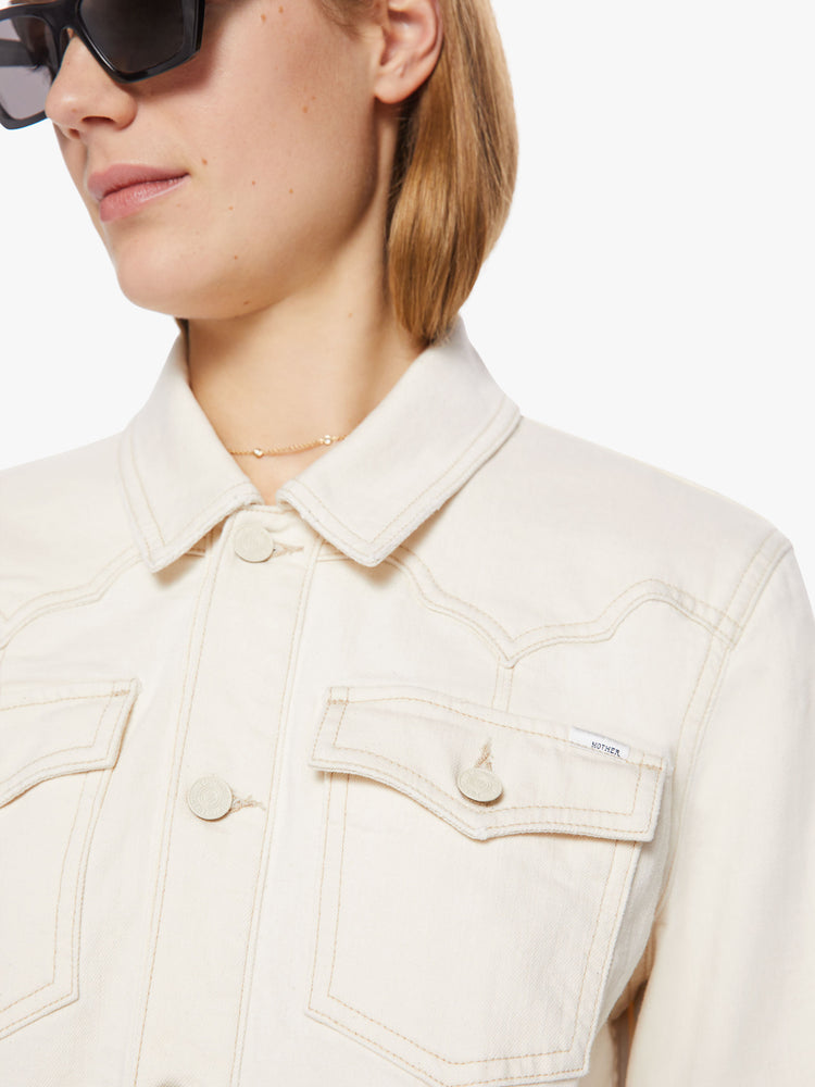 Close up view of woman creamy white classic denim jacket with front patch pockets, a Western-inspired yoke and a boxy fit.
