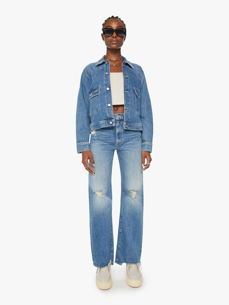 Full body view of a woman boxy denim jacket with Western-inspired stitching across the chest, drop shoulders and oversized patch pockets in a med blue wash.