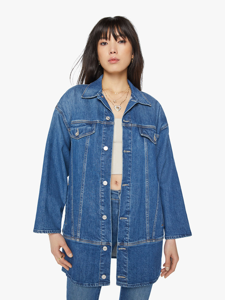 Front view of a woman elongated denim jacket with drop shoulders, boxy wing sleeves and a curved, thigh-length hem in classic blue wash.
