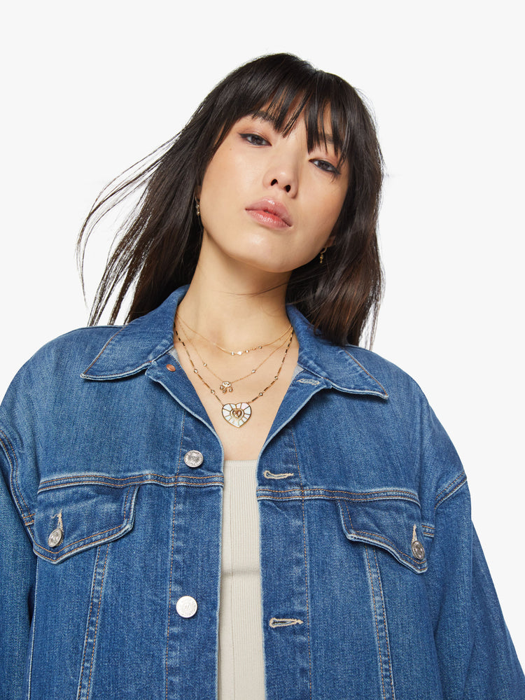 Close up view of a woman elongated denim jacket with drop shoulders, boxy wing sleeves and a curved, thigh-length hem in classic blue wash.