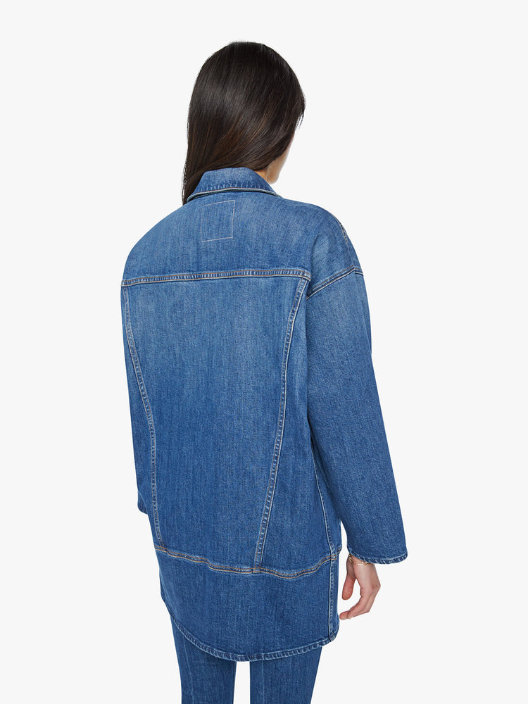 Back view of a woman elongated denim jacket with drop shoulders, boxy wing sleeves and a curved, thigh-length hem in classic blue wash.