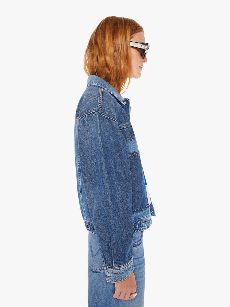 Side view of a woman mid blue denim jacket with drop shoulders, patch pockets and an elastic hem at the waist with darker details on chest.