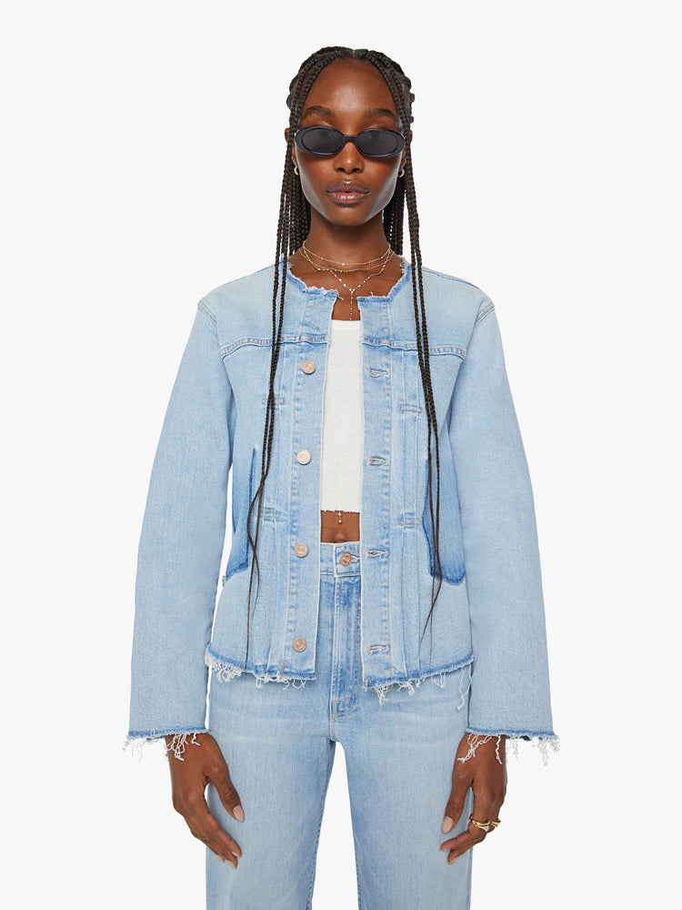 Front view of a women distressed denim jacket is designed with a crewneck, patch pockets, pleated details and raw, frayed hems in a light blue wash with missing patch pockets.