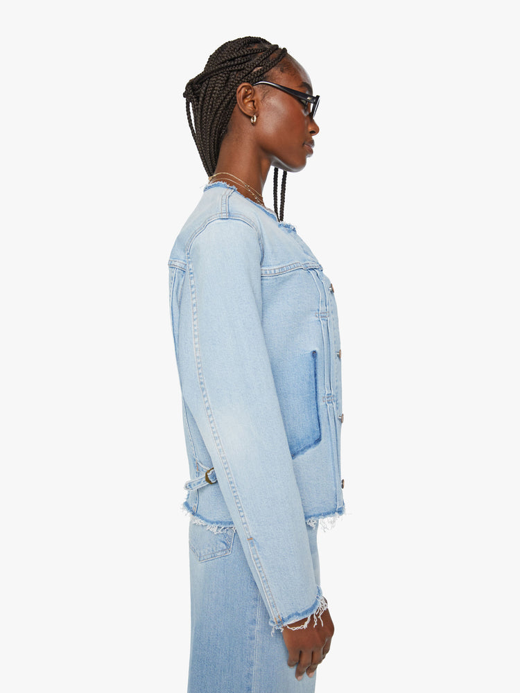Side view of a women distressed denim jacket is designed with a crewneck, patch pockets, pleated details and raw, frayed hems in a light blue wash with missing patch pockets.
