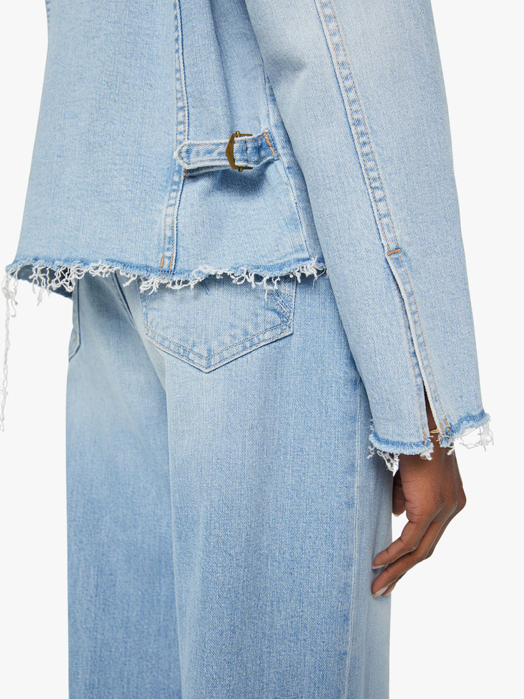 Hem jacket view of a women distressed denim jacket is designed with a crewneck, patch pockets, pleated details and raw, frayed hems in a light blue wash with missing patch pockets.