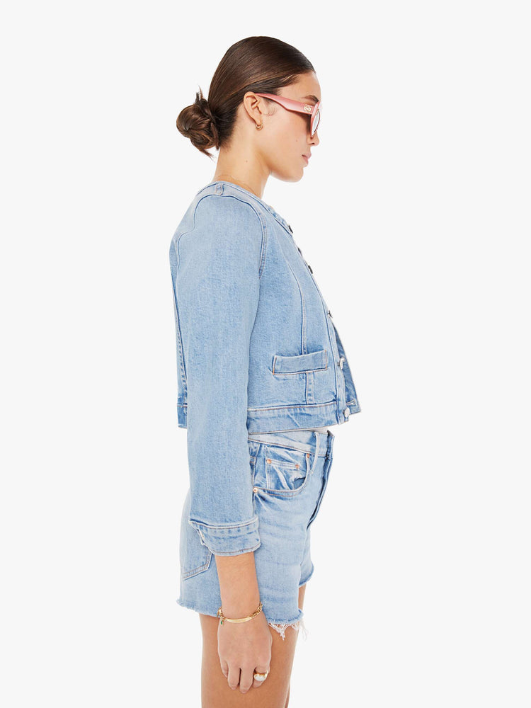 Side view of a light blue wash denim jacket featuring a curved crew neck and a cropped fit.