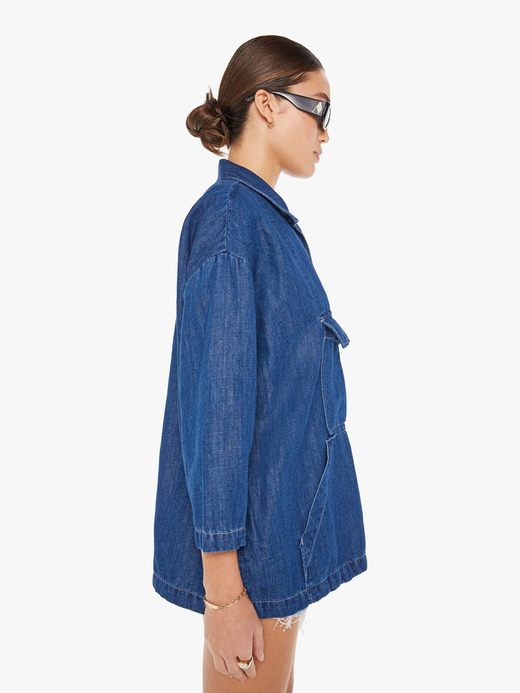 Side view of a womens dark blue denim jacket poncho featuring an open collar neck, cropped sleeves, and a front kangaroo pocket.