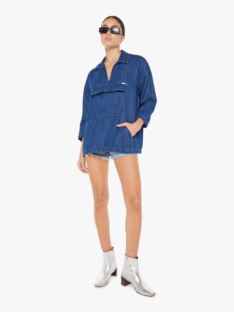 Front full body view of a womens dark blue denim jacket poncho featuring an open collar neck, cropped sleeves, and a front kangaroo pocket.