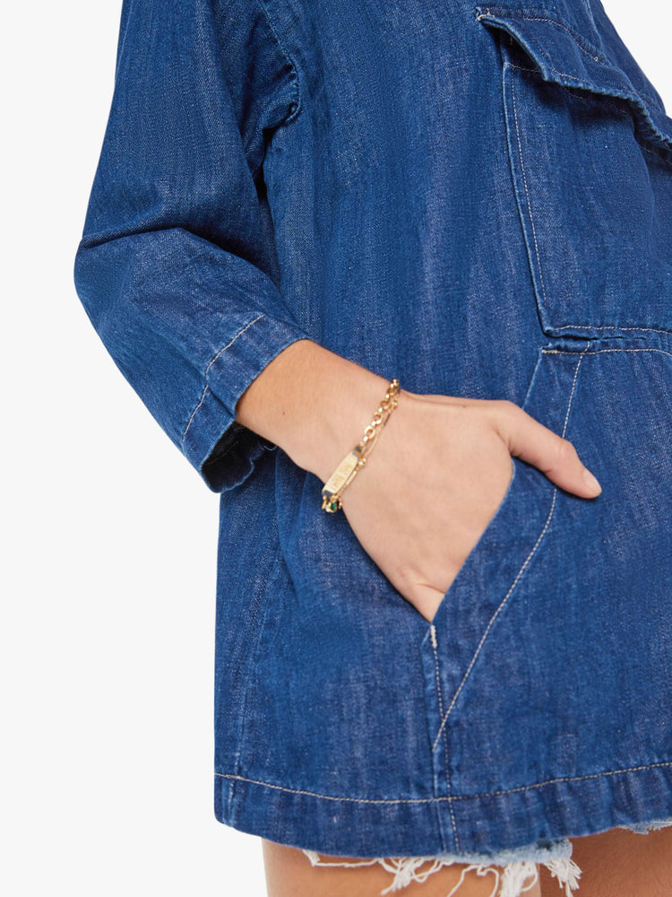 Side close up view of a womens dark blue denim jacket poncho featuring an open collar neck, cropped sleeves, and a front kangaroo pocket.