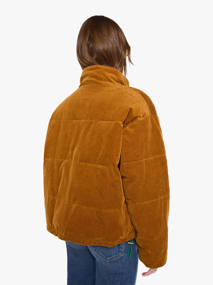 Back view of a woman in a  golden-brown corduroy on one side and a teal-green fabric on the other with oversized printed flowers, gems, and creatures throughout oversized puffer.