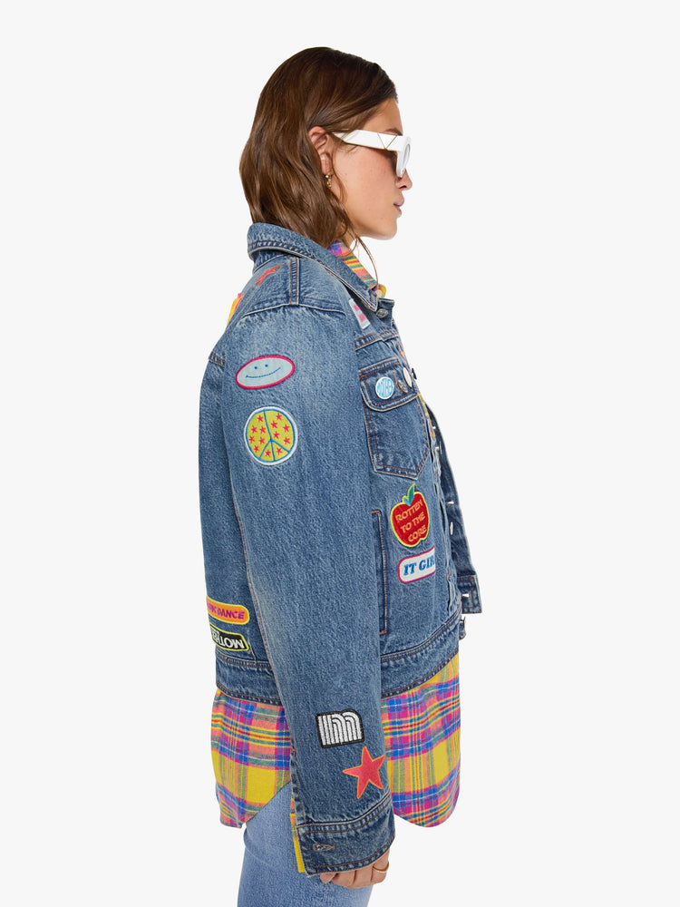 Side view of a woman in a mid blue with vintage patches oversized denim jacket with front patch pockets, drop shoulders, pleated details and a slightly cropped, boxy fit.