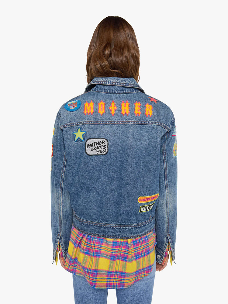 Back view of a woman in a mid blue with vintage patches oversized denim jacket with front patch pockets, drop shoulders, pleated details and a slightly cropped, boxy fit.