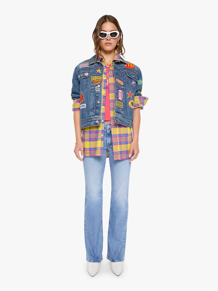 Front full body view of a woman in a mid blue with vintage patches oversized denim jacket with front patch pockets, drop shoulders, pleated details and a slightly cropped, boxy fit.