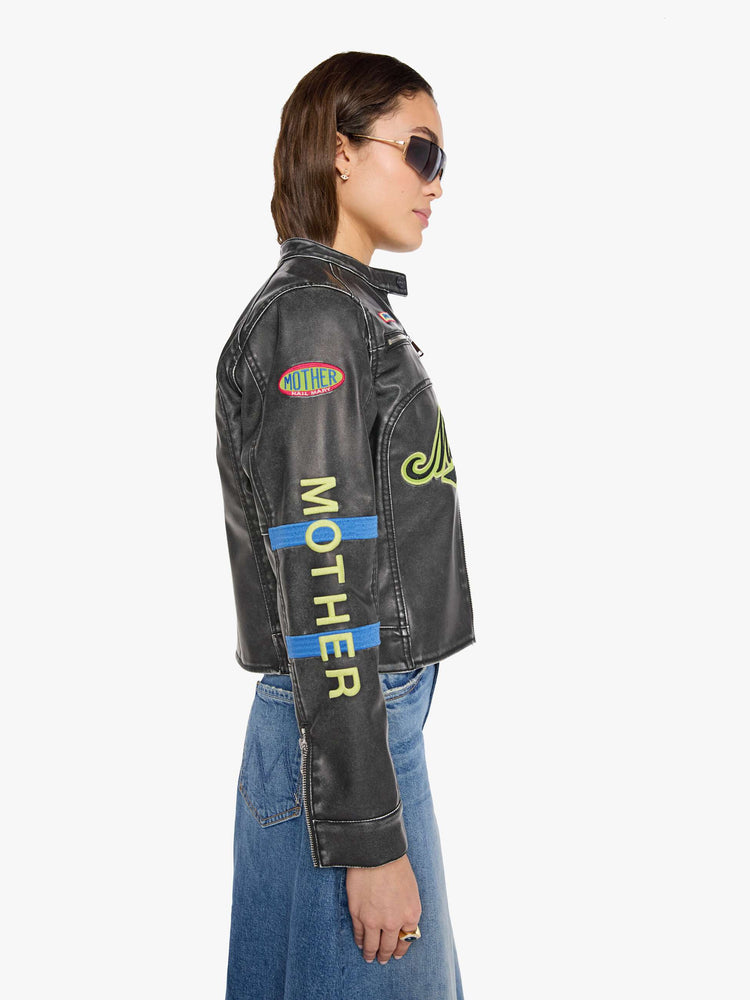 Left side view of a woman in faux black leather with patches jacket with a button-tab crewneck, zip pockets, seamed details, a zip closure and a cropped fit.