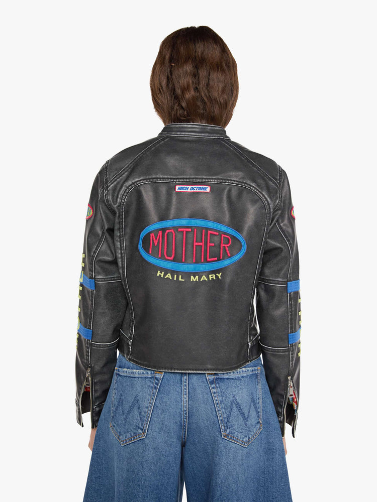Back view of a woman in faux black leather with patches jacket with a button-tab crewneck, zip pockets, seamed details, a zip closure and a cropped fit.