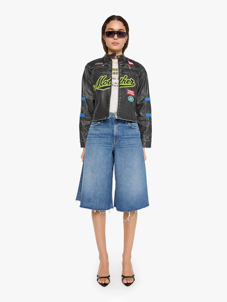 Full body view of a woman in faux black leather with patches jacket with a button-tab crewneck, zip pockets, seamed details, a zip closure and a cropped fit.